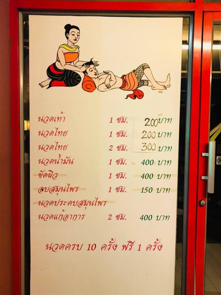 A menu sign outside a Thai massage shop listing services and prices in both Thai and English.